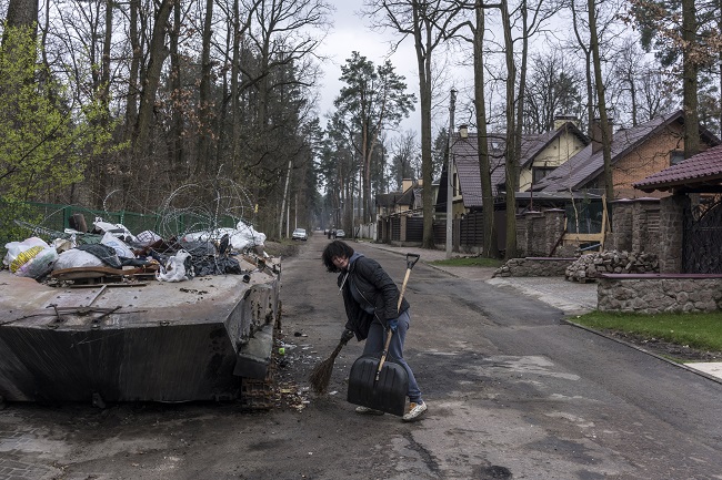 A woman who gave her name only as Nadiya sweeps up around a destroyed Russian armored personnel carrier that has been converted into a dumpster on Thursday, April 21, 2022 in Irpin, Ukraine. Photo Credit:  Brendan Hoffman